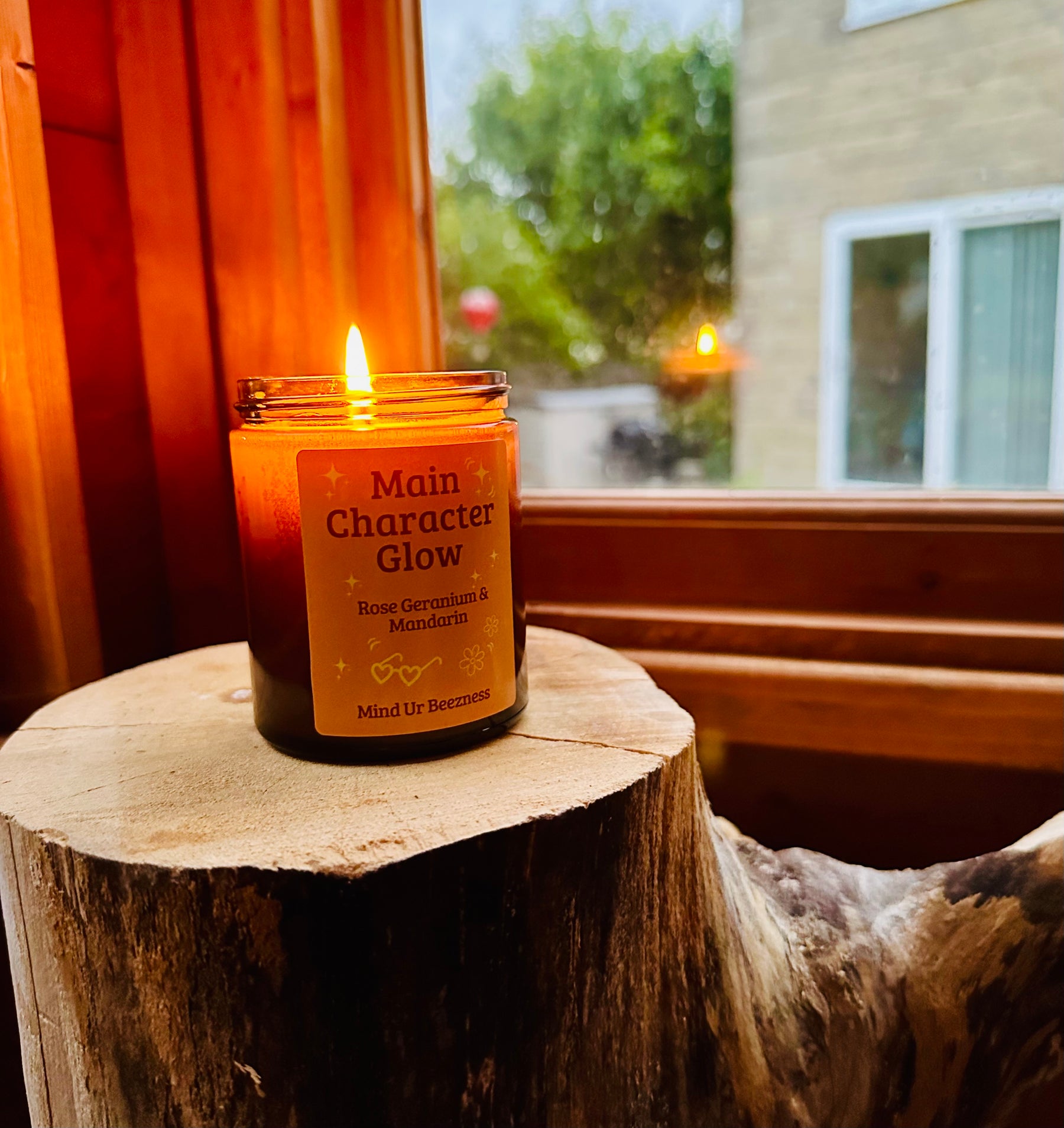 Candle labeled 'Main Character Glow' on a wooden stump with a window and outdoor view in the background