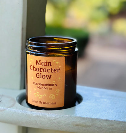 Amber jar candle with “Main Character Glow” label by Mind Ur Beezness, rose geranium and mandarin scent, soft girl aesthetic gift
