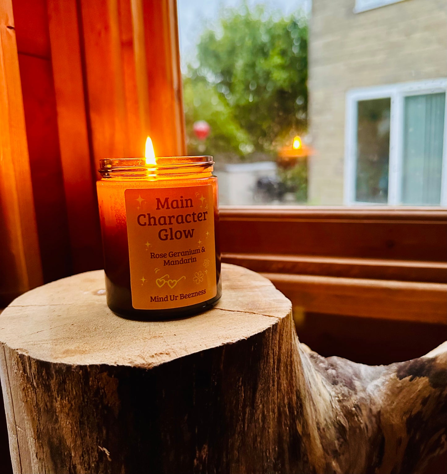 Candle labeled 'Main Character Glow' on a wooden stump with a window and outdoor view in the background