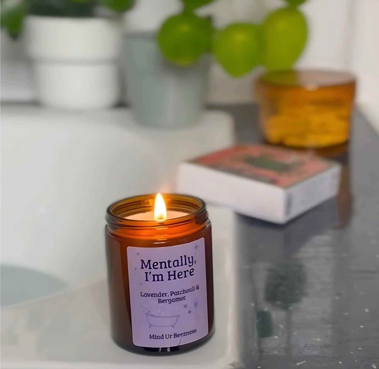 The “Mentally, I’m Here” lavender patchouli bergamot candle by Mind Ur Beezness, softly glowing by the bath in a peaceful soft girl bathroom scene.
