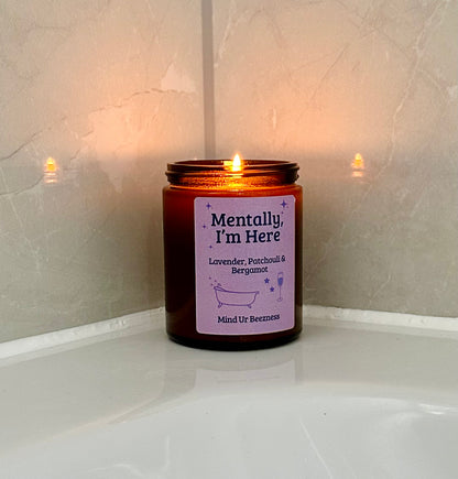 Mind Ur Beezness “Mentally, I’m Here” candle with Lavender, Patchouli & Bergamot, lit beside a white bathtub, casting a soft reflection on glossy bathroom tiles.