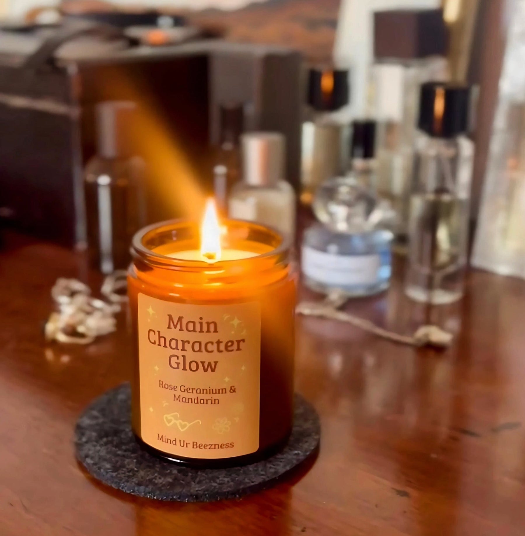 A glowing “Main Character Glow” soft girl era candle by Mind Ur Beezness, styled on a wooden vanity surrounded by elegant perfumes.
